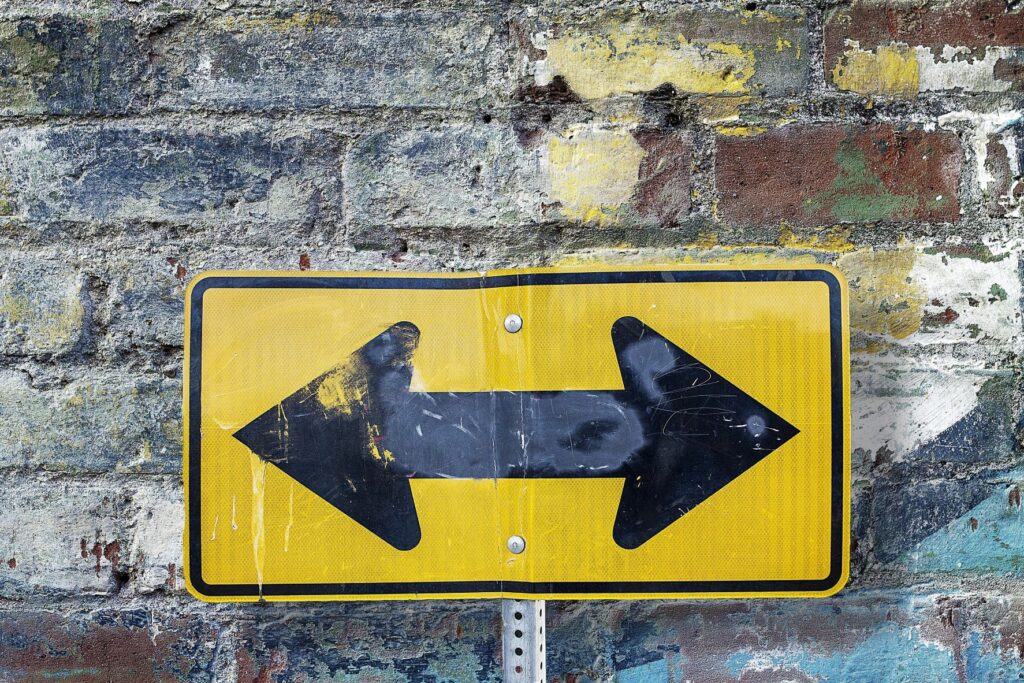 Slightly dented road sign showing an arrow with one head pointing left and another head pointing right