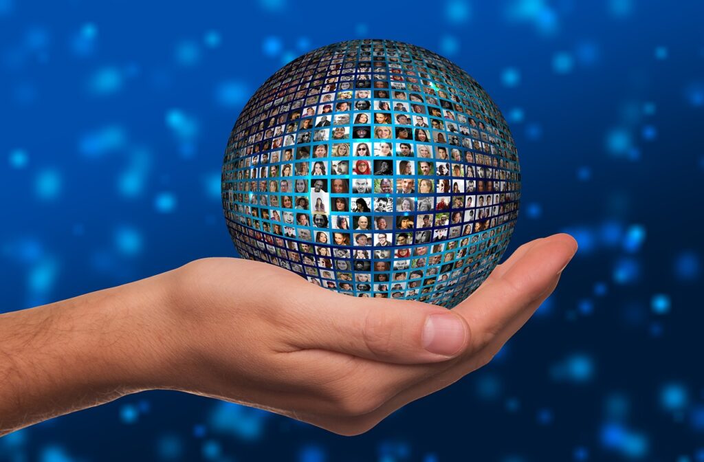 open hand that is cupping a sphere that is made up of dozens of tiny faces of people, such as you might see on a video call. Background is blue with abstract light blue fuzzy elements