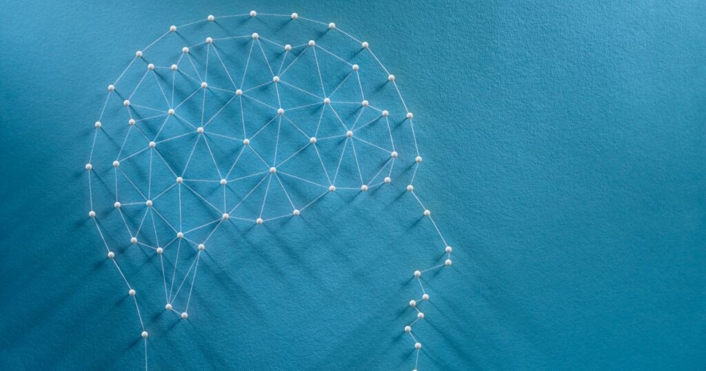 Overhead view of an array of pins stuck into a light-blue board, with white thread connecting neighbouring pins - the pattern makes the outline of a head and a brain (with the brain full of pin-dots connected to each other by thread in an array of little triangles