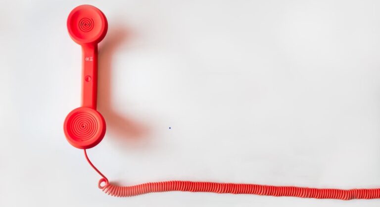 A bright red old fashioned landline telephone handset with curly cord